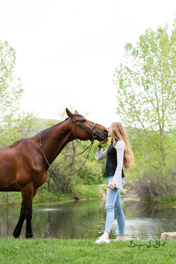 girl kissing horse on the nose by a lake